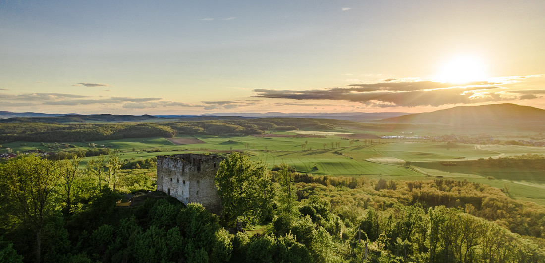 Gründe Landschaft, untergehende Sonne und im Vordergrund ein kleiner Turm auf einem Hügel