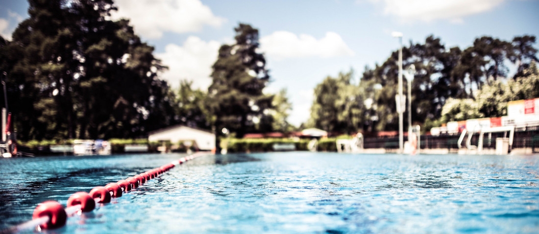 Ein Freibadbecken mit türkisem Wasser und grünen Bäumen im Hintergrund