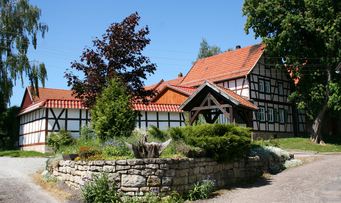 Ein großes Fachwerkhaus mit einer Brunnenlage und einer groben Steinmauer im Vordergrund
