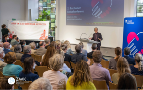 Franz Müntefering auf einer Bühne vor Publikum. Im Hintergrund ein Banner mit dem Logo der Stadt Bochum.