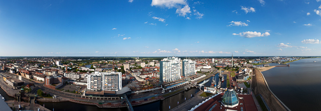 Panoramaaufnahme von Bremerhaven: rechts ist Wasser zu sehen, mittig weiße Hochhäuser und die Stadt..