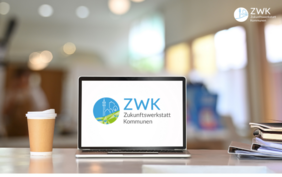 offener Laptop mit ZWK Logo, Kaffeebecher und Akten