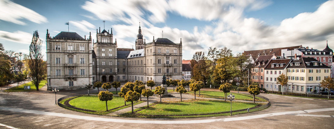 Panoramabild vom Schlossplatz in Coburg, eine Wiese, Häuser im Hintergrund und verzerrte Wolken am Himmel.