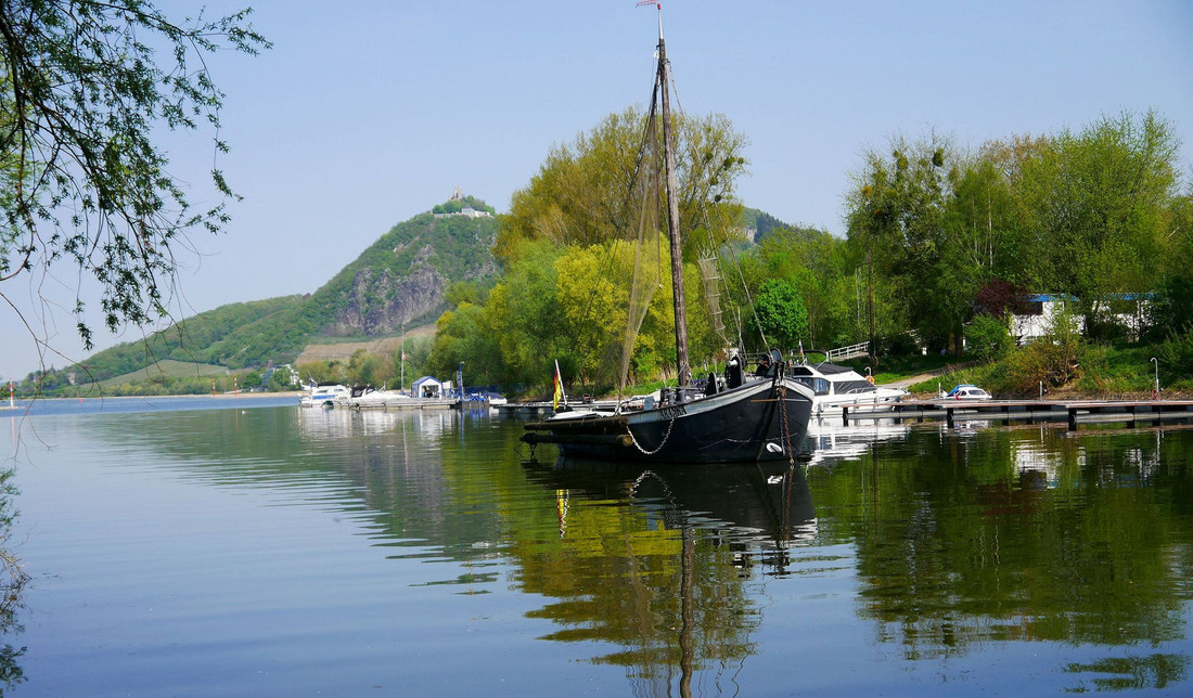 Blaues Wasser, ein schwarzes Segelboot und im Hintergrund ein Berg