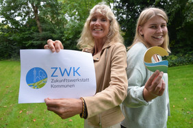 zwei blonde Frauen halten das ZWK Logo und das Geestland Logo in die Kamera