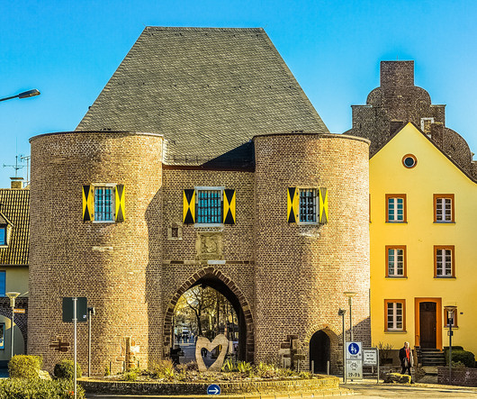 Großes Tor aus Backsteinen, mit zwei Türmen und einem konischen Dach. Gelb-schwarze Fensterläden und ein großes geschnitztes Herz auf dem Vorplatz.