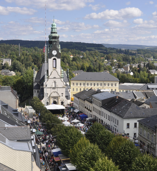 Ein begrünter Marktplatz von oben mit vielen Menschen und einer großen Kirche.