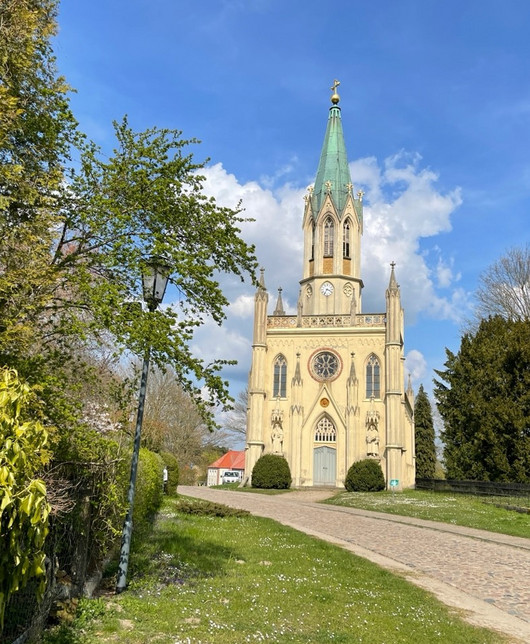 neogotische Kirche, ein Kiesweg, Wiesen und Bäume