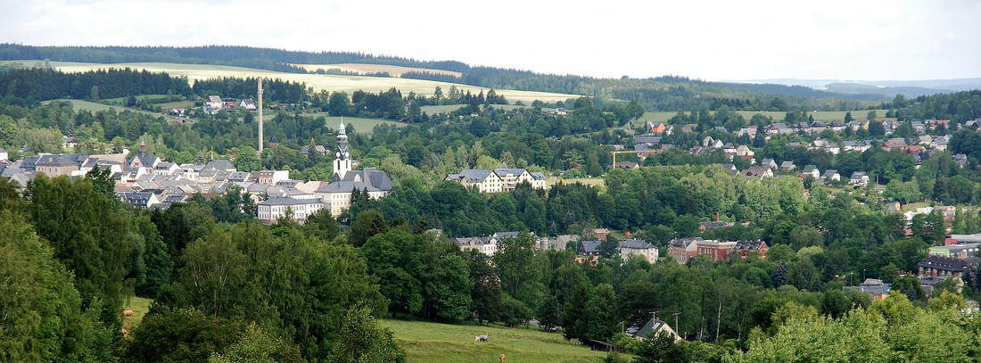 kleine Stadt mit Kirchturm umgeben von grünen Feldern und Hügeln