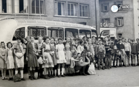 Historisches Bild in schwarz-weiß. Mehrere Dutzend Kinder stehen für ein Foto vor einem Bus. Hinter dem Bus ist ein großes Gebäude zu sehen.