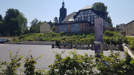 Ein Fachwerkhaus und ein Restaurant an einem gepflasterten Platz mit Begrünung