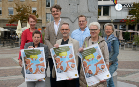 Drei Männer und vier Frauen stehen auf einem Platz und halten drei Plakate zum Seniorentag in die Kamera