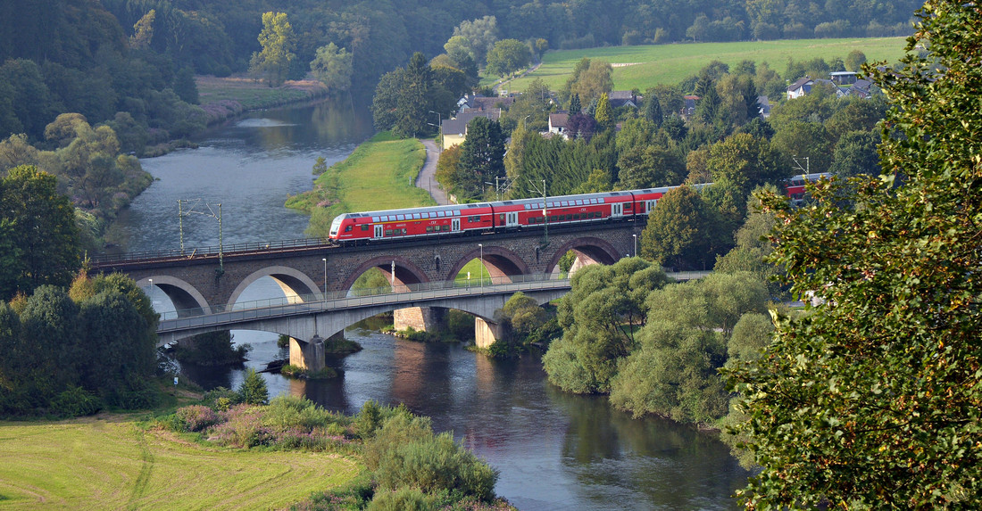 Ein Viadukt mit Bahngleisen und Zug über einem Fluss in idyllischer Landschaft