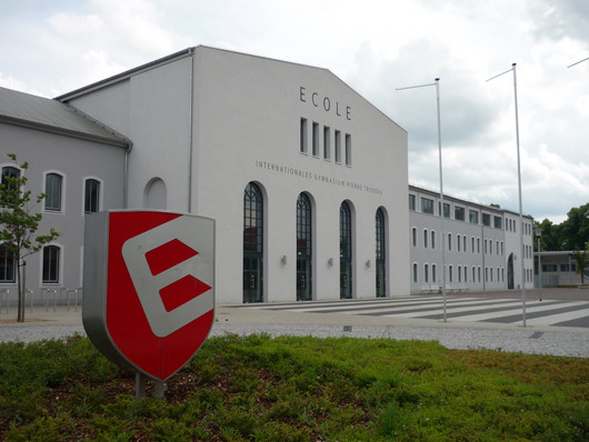 Rotes Schild vor weißem Gebäude: ECOLE Gymnasium