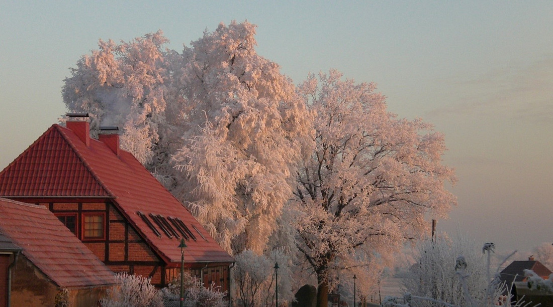 Ein rotes Fachwerkhaus im Winter. Daneben eine Landstraße und ein großer Baum mit weißgefrorenen Blättern.