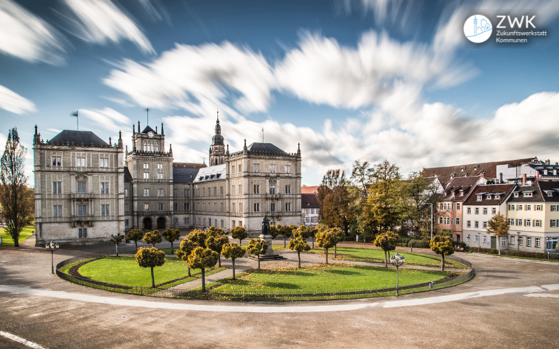 Panoramabild vom Schlossplatz in Coburg, eine Wiese, Häuser im Hintergrund und verzerrte Wolken am Himmel.