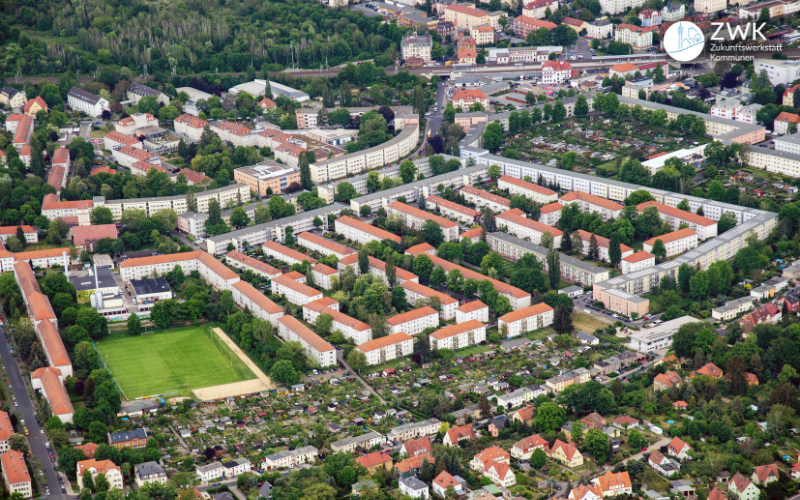 Luftbild mit einem sehr großen Gebäudekomplex mit rotem Dach. Rundherum Bäume und Felder.