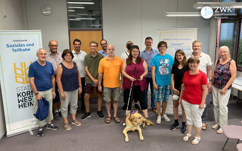 15 Menschen und ein Hund lächeln in die Kamera. Links im Bild ein Roll-Up der Stadt Kornwestheim.