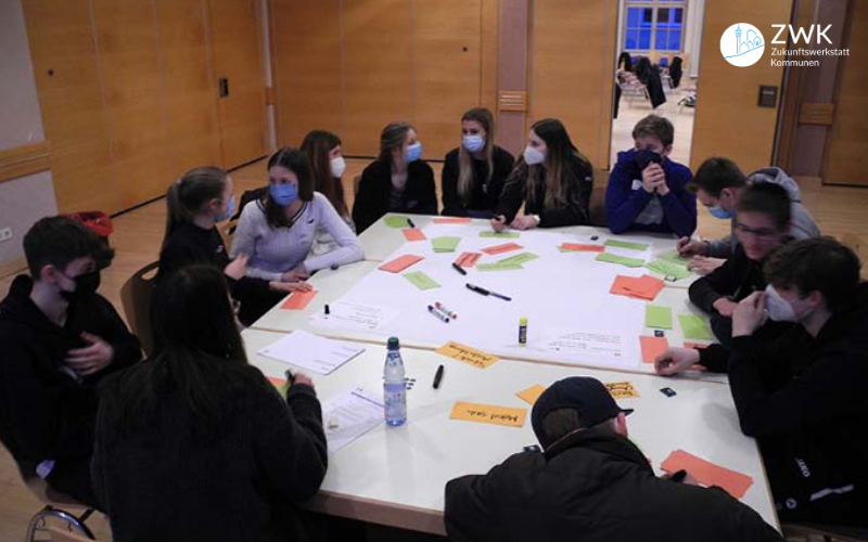 Eine Gruppe von Jugendlichen sitzt um einen Tisch und diskutiert