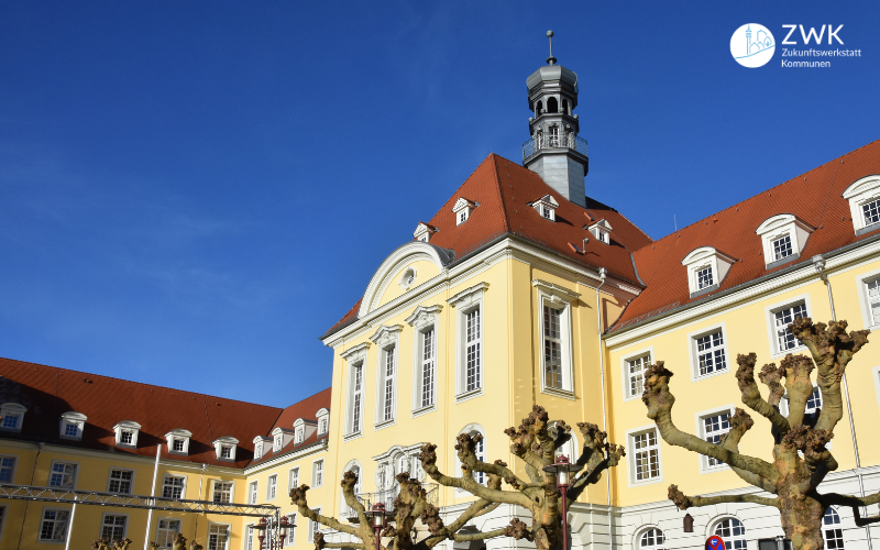 Rathaus Herford - großes gelbes Gebäude mit rotem Ziegeldach und geschnittenen Weiden auf dem Vorplatz