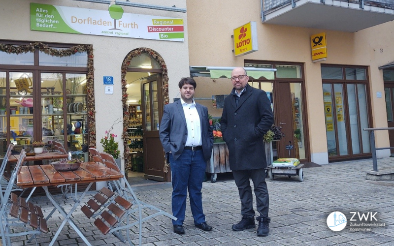 Zwei Männer stehen in der Fußgängerzone vor einem Dorfladen.